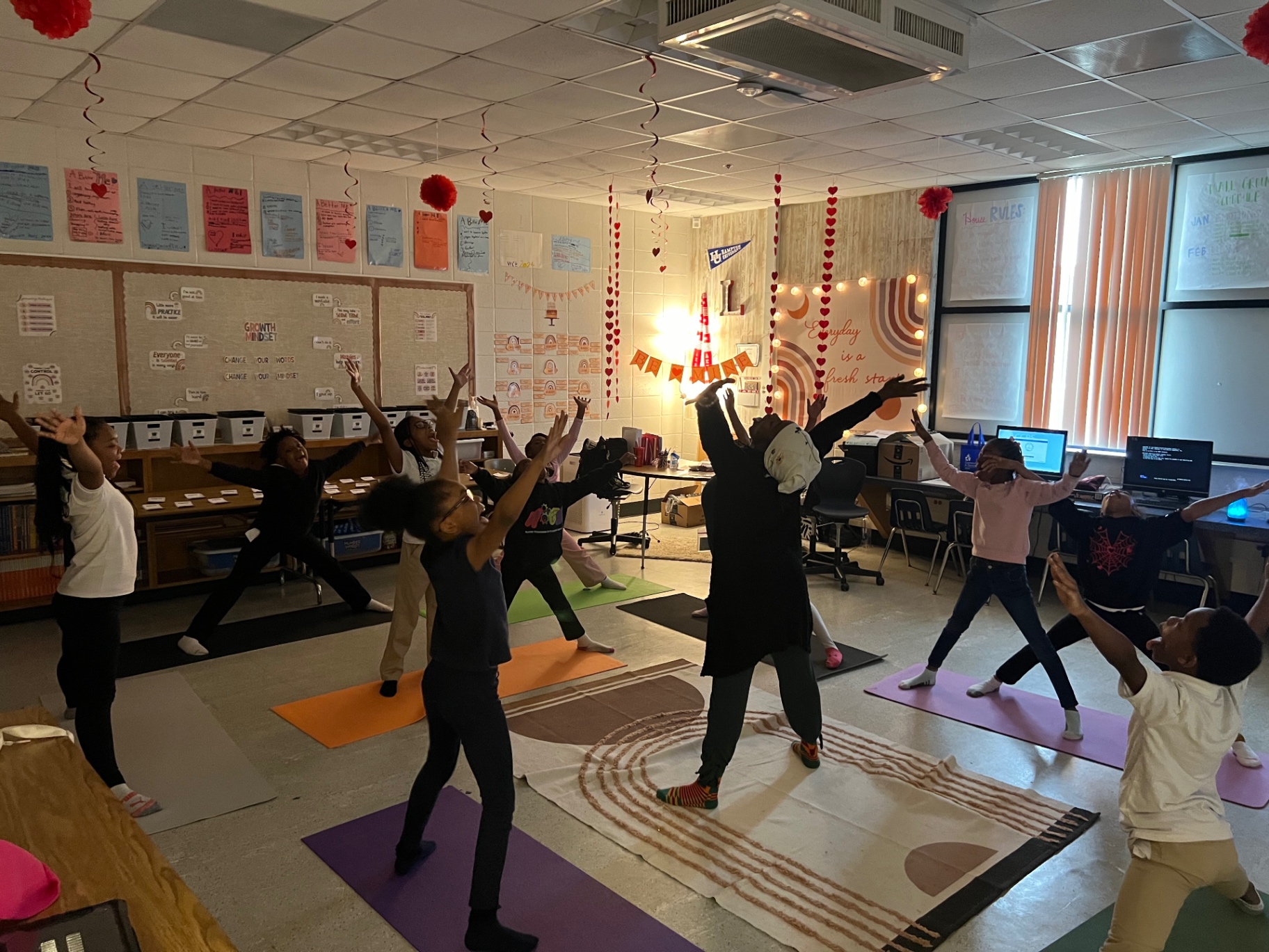 A classroom of children reaching wide overhead together on colorful mats