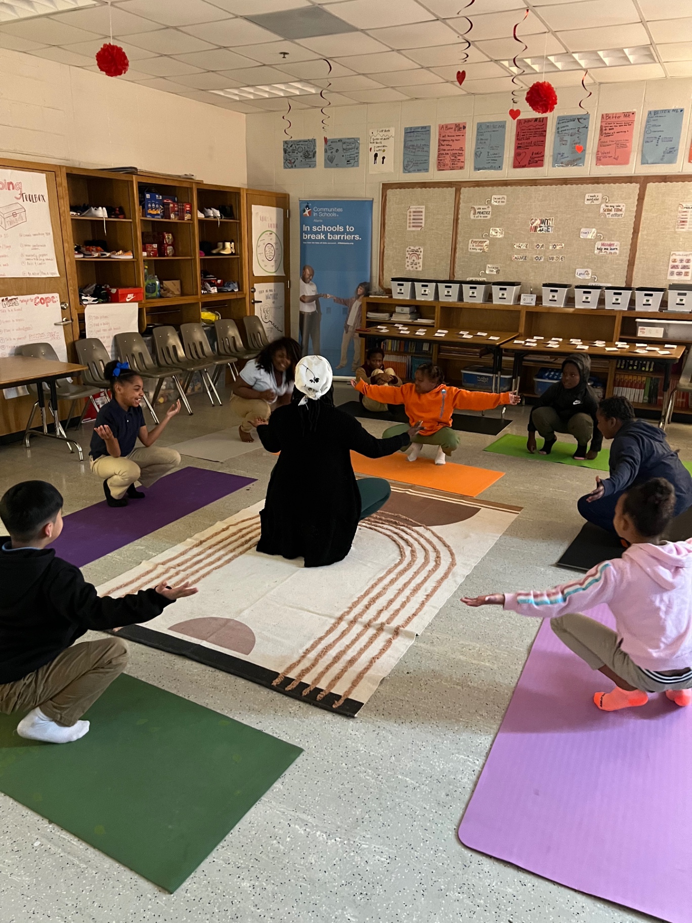 A seated circle on mats with arms opened wide, facilitator in the center