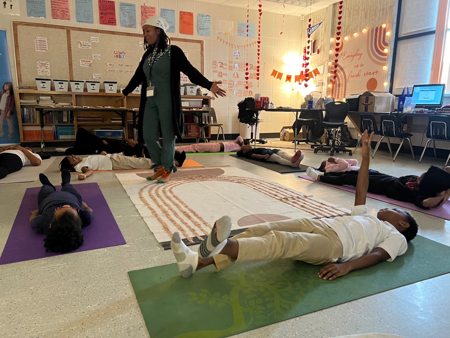 Children resting on their backs on mats while the facilitator walks the room